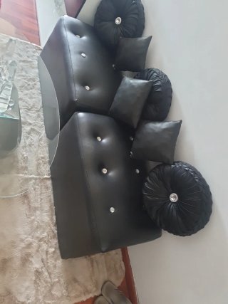 Divano in pelle sintetica nera con cuscini e tavolino.